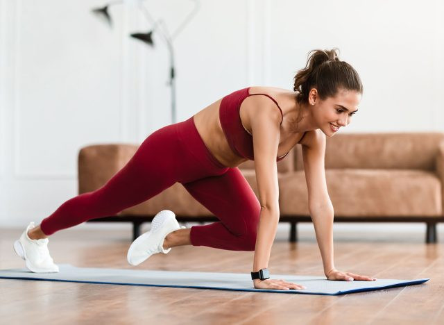 7 Động Tác Đốt Cháy Mỡ Bụng Và Tăng Cơ Nhanh Hơn Cả Chạy Bộ Smiling Sporty Woman Training At Home In Living Room In Front Of Laptop, Beautiful Female Doing Cross Body Mountain Climbers Exercise Looking At Screen Having Online Video Call With Trainer Instructor