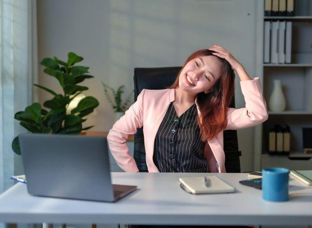 Nữ quản lý châu Á nghỉ giải lao và duỗi cổ khi ngồi tại bàn làm việc trong văn phòng hiện đại