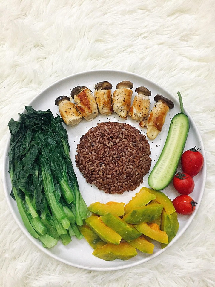 Cơm gạo lứt ăn cùng ức gà cuộn nấm đùi gà áp chảo, rau cải ngọt luộc, bí đỏ luộc, cà chua, dưa leo.