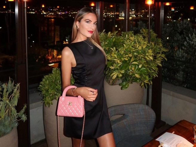 Model Pamela Genini poses with a pink Chanel purse at an outdoor restaurant at night.