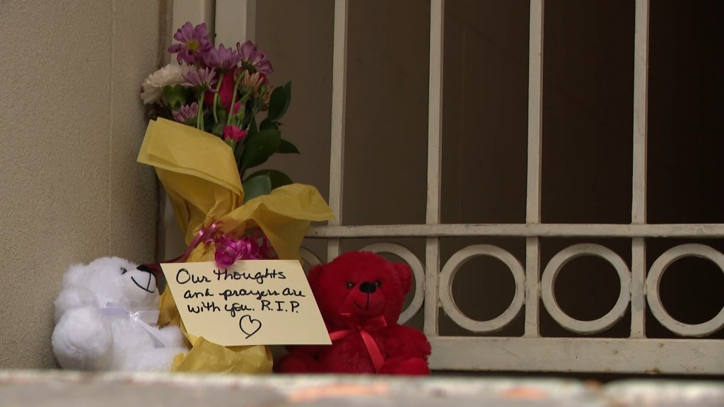 A memorial with flowers, two teddy bears, and a handwritten note that reads,